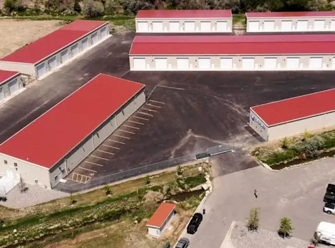 Aerial view of SYT Storage: steel storage buildings with red metal roofs arranged around a large paved lot inside a security fence