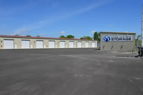 Large paved lot at SYT Storage with a row of overhead doors and the Store Your Toys Storage sign